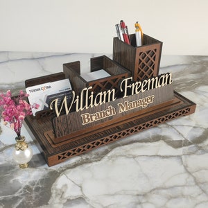 May include: Wooden desk organizer with a pen holder, note pad holder, and business card holder. The organizer has a personalized nameplate that reads "William Freeman Branch Manager".