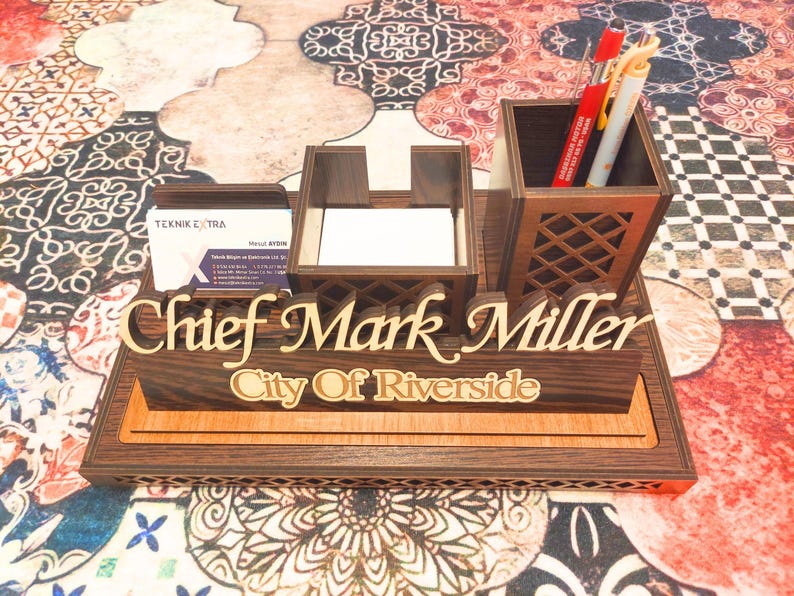 May include: A wooden desk organizer with a nameplate that reads "Chief Mark Miller City of Riverside". The organizer has a pen holder, a business card holder, and a note pad holder.