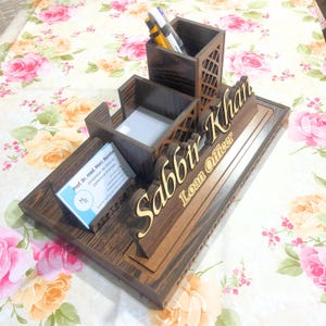 May include: A wooden desk organizer with a nameplate that reads "Sabbir Khan Loan Officer". The organizer has compartments for pens, pencils, and business cards.