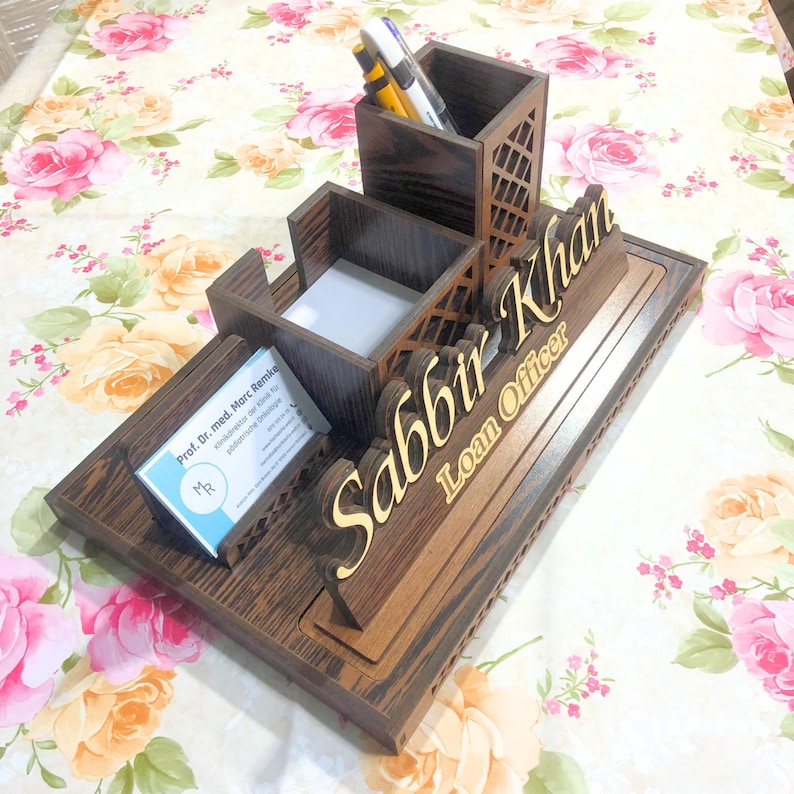 May include: A wooden desk organizer with a nameplate that reads "Sabbir Khan Loan Officer". The organizer has compartments for pens, pencils, and business cards.