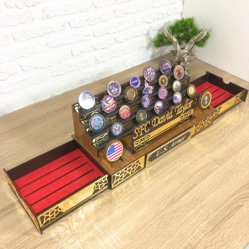Op de afbeelding: Een houten displaykast met een lade bekleed met rood vilt. De kast is ontworpen om een ​​collectie challenge-munten te bewaren en te presenteren. De kast heeft een naamplaatje met de tekst "SFC David Taylor" en een plaquette met de tekst "U.S. Army".