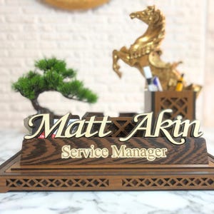 May include: Wooden desk nameplate with the name "Matt Akin" and the title "Service Manager" in gold lettering. The nameplate is on a wooden base with a decorative lattice design.
