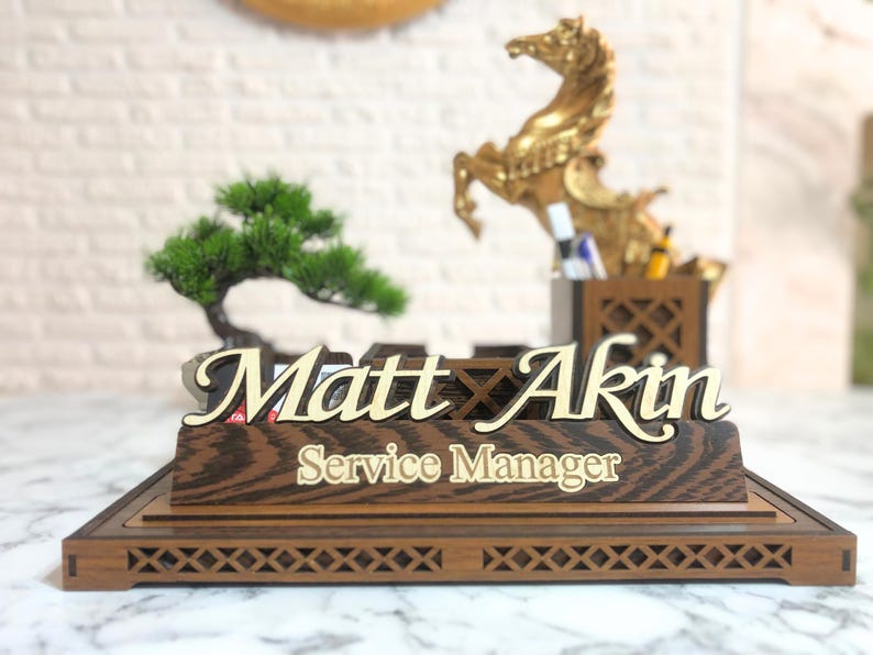 May include: Wooden desk nameplate with the name "Matt Akin" and the title "Service Manager" in gold lettering. The nameplate is on a wooden base with a decorative lattice design.