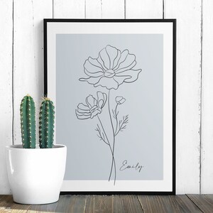 May include: A black framed print with a light blue background featuring a line drawing of a flower with the name "Emily" written below.
