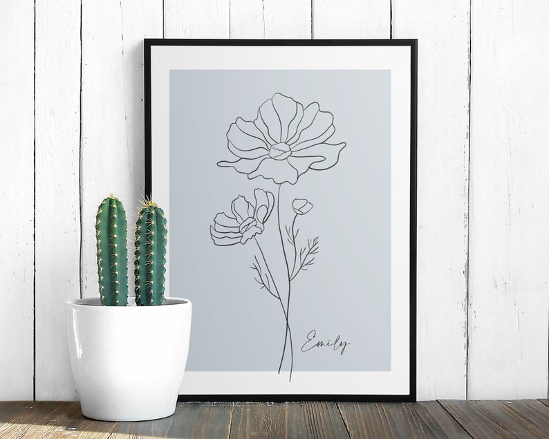 May include: A black framed print with a light blue background featuring a line drawing of a flower with the name "Emily" written below.