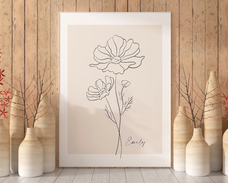 May include: A minimalist line art print of a flower with the name "Emily" written below. The print is framed in a white frame and is displayed against a wood background.