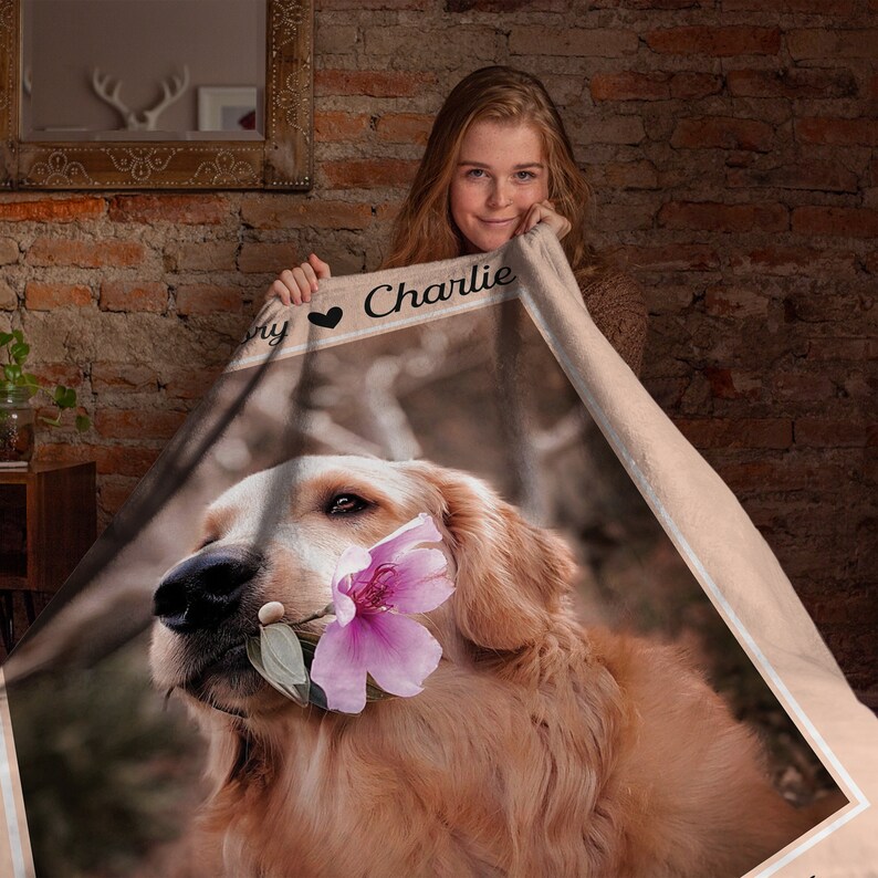 May include: A soft, beige fleece blanket with a photo of a golden retriever dog holding a pink flower in its mouth. The blanket has the text "My Charlie" with a heart symbol.
