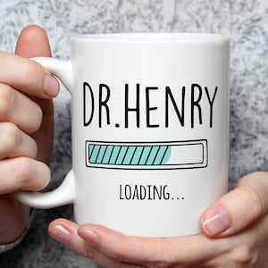 May include: White ceramic mug with black text that reads "DR. HENRY" and a blue progress bar that says "LOADING..." underneath.