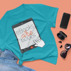 Puede incluir: Una camiseta azul turquesa con un gráfico de una pantalla de tableta que dice "eBooks are books" en texto blanco con la palabra "are" en naranja. Una mano está apuntando a la pantalla.