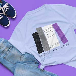 Könnte beinhalten: Ein hellblaues T-Shirt mit einer Grafik von gestapelten Büchern in den Farben der asexuellen Pride-Flagge. Der Text "happily ever after" ist unter den Büchern gedruckt.