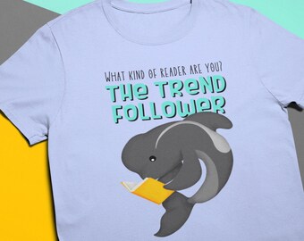 May include: A light blue t-shirt with the text "What kind of reader are you? The Trend Follower" in black and teal. A cartoon gray whale with a yellow book is reading.