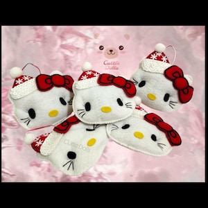 May include: A collection of white felt cat-shaped ornaments featuring red bows, yellow noses, and black whiskers. Each ornament wears a red and white Santa hat with snowflake patterns and white trim. The text Cuttie Dolls is visible on one.