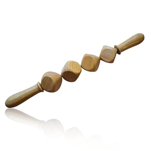 Puede incluir: Un rodillo de masaje de madera con cuatro botones cuadrados redondeados conectados. El rodillo tiene un mango de madera.