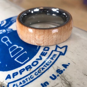 May include: A wooden ring with a silver band. The wood is a light brown color and has a smooth finish. The silver band is polished and shiny.