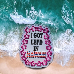 May include: A white oval-shaped sticker with a pink floral border. The sticker says "I GOT LEI'D IN HAWAII" with the word "HAWAII" in the colours of the Hawaiian flag.