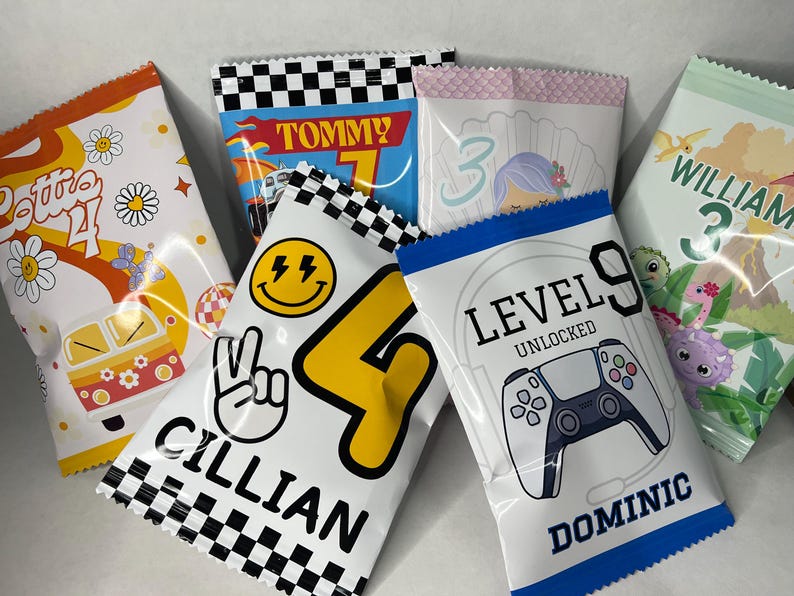 May include: Nine colorful party favor bags with different designs and names. The bags feature a variety of themes, including a car, a smiley face, a video game controller, a mermaid, and a dinosaur. The bags are all decorated with colorful patterns and text.