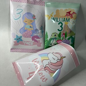May include: Three pink and white treat bags with different designs. One bag features a mermaid with the name "Faith" and the number "3". Another bag features a dinosaur with the name "William" and the number "3". The third bag features a unicorn with the name "Willow" and the number "4".