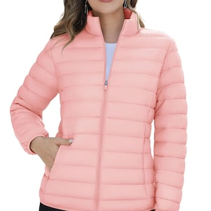 May include: A light pink puffer jacket with a high collar and a full-length zipper. The jacket has a quilted design and two side pockets. The model is wearing a white shirt underneath. The jacket is a lightweight outerwear option.