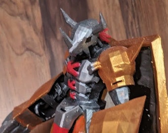 May include: A detailed figurine of a Digimon character, featuring a metallic silver and gold color scheme with red accents. The figure has sharp claws, a shield, and a dynamic pose, standing on a black base. The figurine is held by a hand.