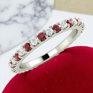 Pu&ograve; includere: Un anello d'argento con pietre preziose rosse e chiare alternate. L'anello &egrave; incastonato con piccoli rubini rotondi e diamanti trasparenti. Le pietre preziose sono disposte in un motivo continuo attorno alla fascia. L'anello &egrave; esposto su una superficie rossa.