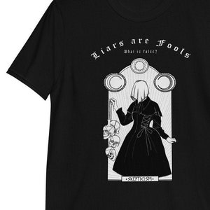 May include: Black t-shirt with a white graphic design featuring a woman in a hooded dress holding a string of skulls. The text "Liars are Fools" is at the top of the design, and "Skepticism" is at the bottom.