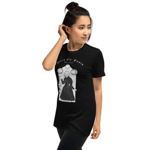 May include: Black t-shirt with a white graphic of a woman in a dress with the text "Liars are Fools" and "What is Truth?" printed on the shirt.