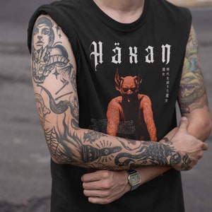 May include: Black sleeveless top with the word "Häxan" in a gothic font. The shirt features a red and orange illustration of a horned figure. The sleeves are rolled up, revealing multiple tattoos on the arms.