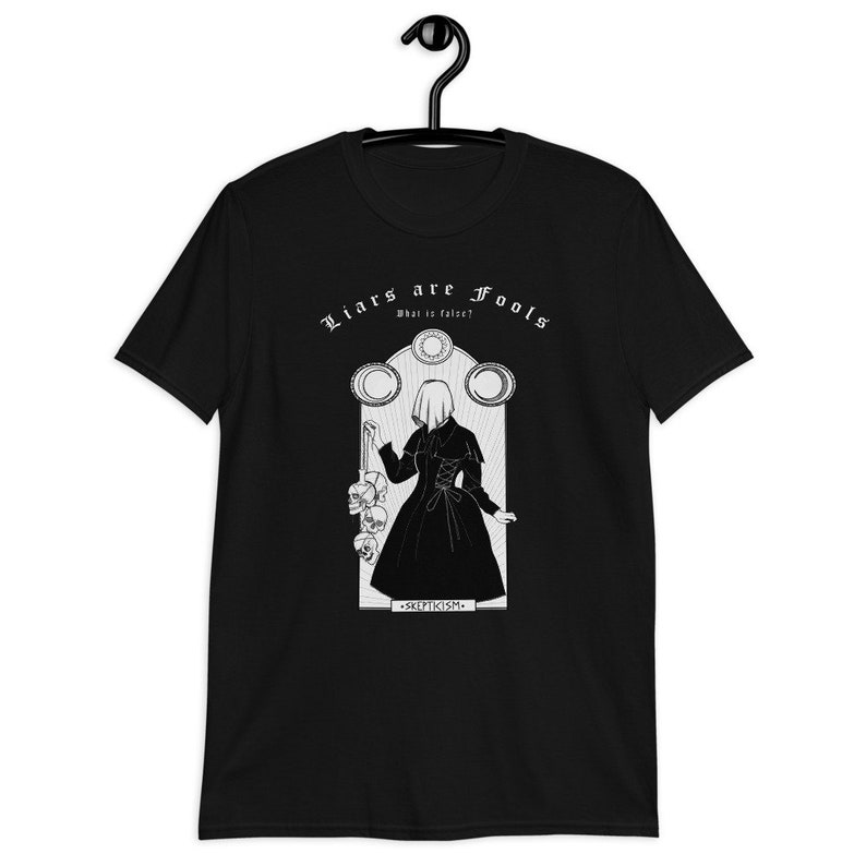 May include: Black t-shirt with a white graphic design featuring a woman in a long dress holding a string of skulls. The text "Liars are Fools" is above the woman and "What is false?" is below. The text "Skepticism" is at the bottom of the graphic.