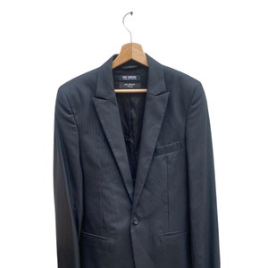 Peut inclure: Un blazer gris foncé avec une fermeture à bouton unique et une étiquette indiquant "RAF SIMONS" à l'intérieur.
