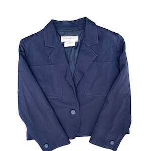 Op de afbeelding: Een marineblauwe blazer met een enkele knoopsluiting en twee klepzakken. De blazer heeft een label met de tekst "Yves Saint Laurent" aan de binnenkant.