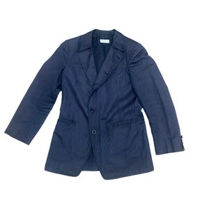 May include: A dark blue blazer with thin white stripes. The blazer has a notched lapel, two button closure, and two flap pockets.