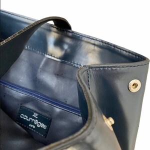 May include: A navy blue leather tote bag with a zippered pocket and a silver metal logo that reads "Courreges Paris".