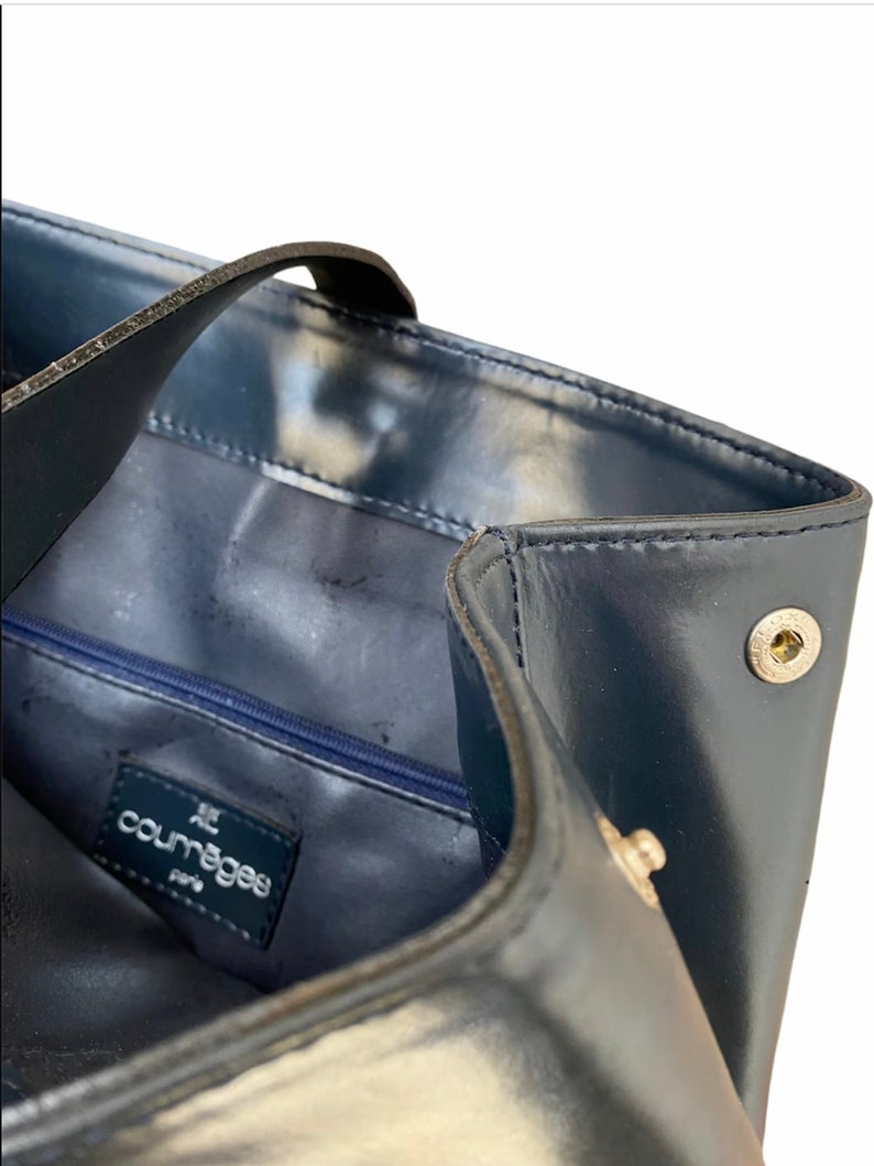 May include: A navy blue leather tote bag with a zippered pocket and a silver metal logo that reads "Courreges Paris".