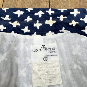 K&ouml;nnte beinhalten: Nahaufnahme des Inneren eines Kleidungsst&uuml;cks mit marineblauem Stoff und einem wei&szlig;en Kreuzmuster. Das Futter ist wei&szlig;. Ein Etikett lautet "courreges paris made in france" und enth&auml;lt Waschanweisungen.