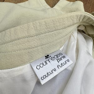 Puede incluir: Primer plano de una prenda verde claro con forro blanco. La etiqueta dice "COURREGES paris couture future" en texto negro. La tela tiene una apariencia texturizada.