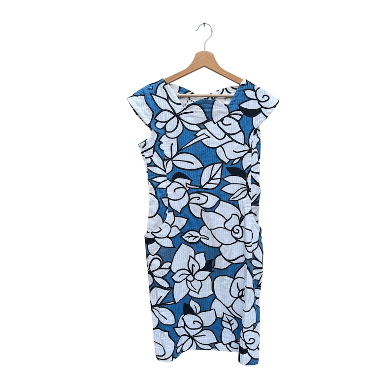 Puede incluir: Un vestido de estampado floral azul y blanco con mangas cortas colgado de una percha de madera.