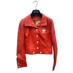 May include: A bright orange leather jacket with a white logo on the front. The jacket has a snap closure and a collar that can be folded up.