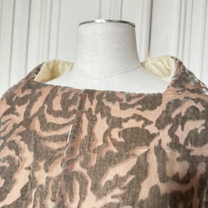 Puede incluir: Primer plano de una prenda con dise&ntilde;o estampado. La tela presenta un patr&oacute;n repetitivo de formas marr&oacute;n oscuro sobre un fondo rosa claro. La prenda est&aacute; drapeada sobre un maniqu&iacute;, mostrando la textura y el dise&ntilde;o.