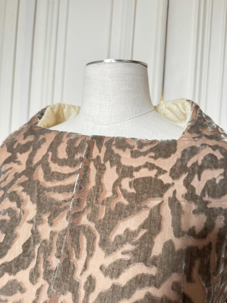 Puede incluir: Primer plano de una prenda con dise&ntilde;o estampado. La tela presenta un patr&oacute;n repetitivo de formas marr&oacute;n oscuro sobre un fondo rosa claro. La prenda est&aacute; drapeada sobre un maniqu&iacute;, mostrando la textura y el dise&ntilde;o.