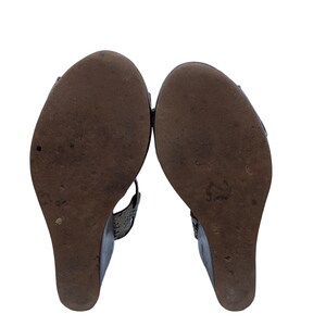 May include: Pair of wedge sandals with dark brown soles and a textured pattern. The uppers are a dark color with a snakeskin-like texture. The wedge heels are approximately 3 inches high.