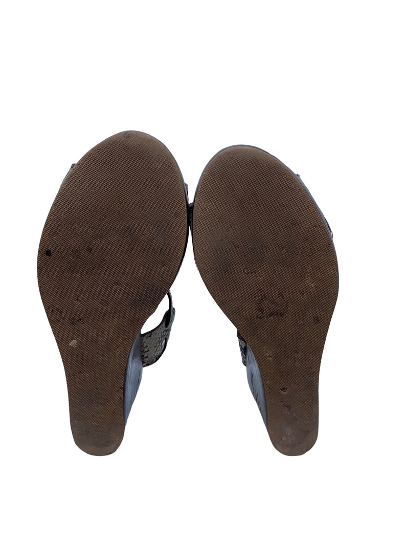 May include: Pair of wedge sandals with dark brown soles and a textured pattern. The uppers are a dark color with a snakeskin-like texture. The wedge heels are approximately 3 inches high.
