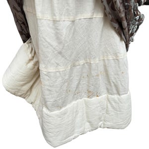 Puede incluir: Prenda de vestir en capas con una base de tela acolchada de color crema. La capa superior es una tela estampada con tonos marrones y una textura aterciopelada. La prenda parece ser una falda o un vestido.