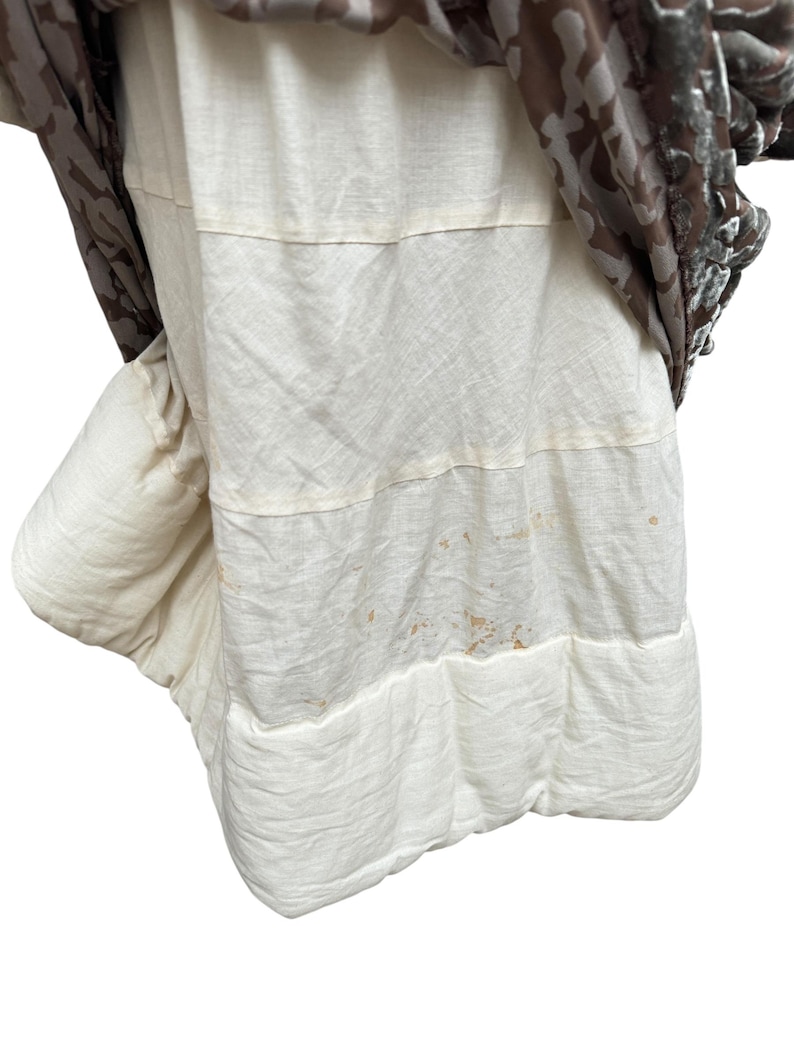 Puede incluir: Prenda de vestir en capas con una base de tela acolchada de color crema. La capa superior es una tela estampada con tonos marrones y una textura aterciopelada. La prenda parece ser una falda o un vestido.