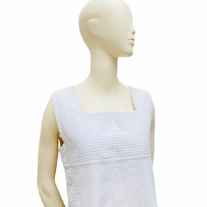 May include: A white sleeveless dress with thin vertical stripes. The dress has a square neckline and a straight silhouette.