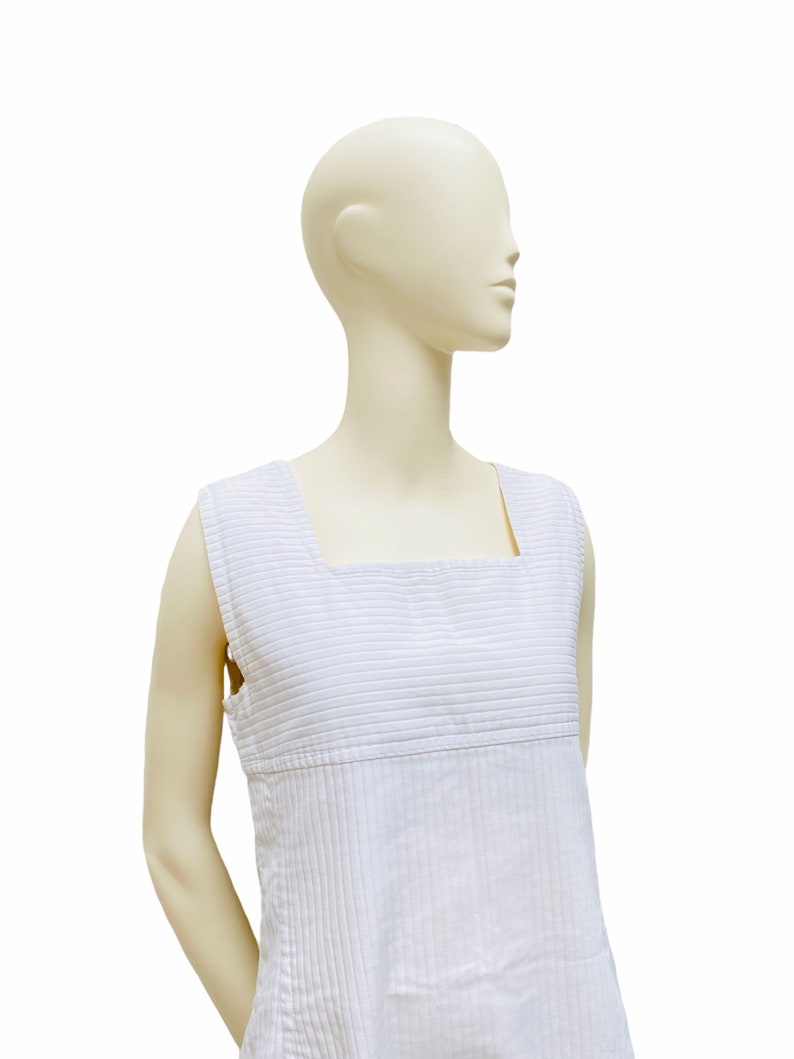 May include: A white sleeveless dress with thin vertical stripes. The dress has a square neckline and a straight silhouette.