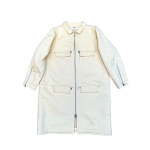 May include: A long, cream-colored jacket with a zipper closure and multiple pockets. The jacket has a collar and long sleeves with zippered cuffs.
