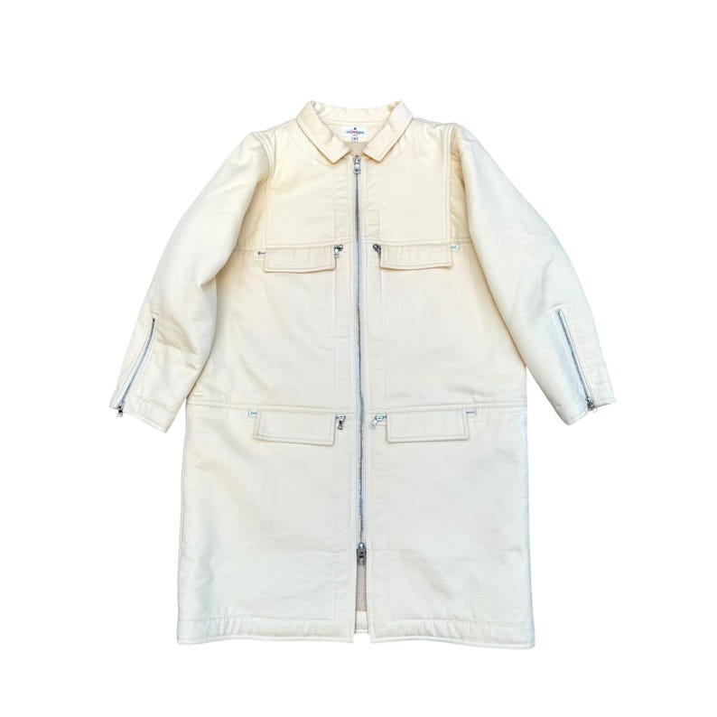 May include: A long, cream-colored jacket with a zipper closure and multiple pockets. The jacket has a collar and long sleeves with zippered cuffs.