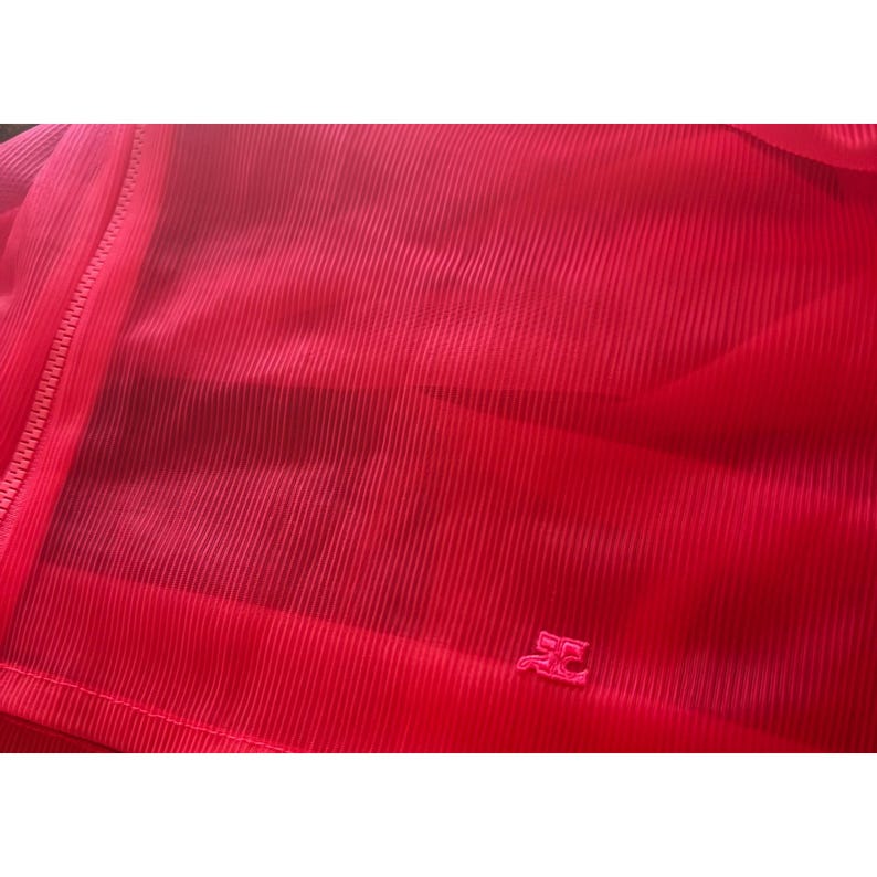 May include: Bright red, ribbed fabric with a zipper and a small logo. The material has a vertical striped texture. The zipper is on the left side of the image. The logo is on the bottom right.