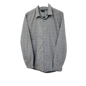 Può includere: Una camicia grigia a maniche lunghe con bottoni e un piccolo motivo bianco. La camicia ha un colletto e una chiusura con bottoni.