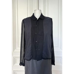 Pode incluir: Camisa preta abotoada com gola redonda. A camisa apresenta mangas compridas e transparentes nas laterais e um painel central liso. A pe&ccedil;a &eacute; exibida em um manequim, mostrando seu ajuste e design sob medida.